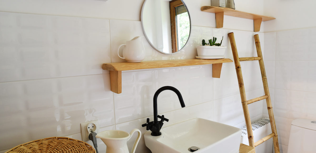 Small bathroom with white tile walls, light wood accents, and round hanging mirror.