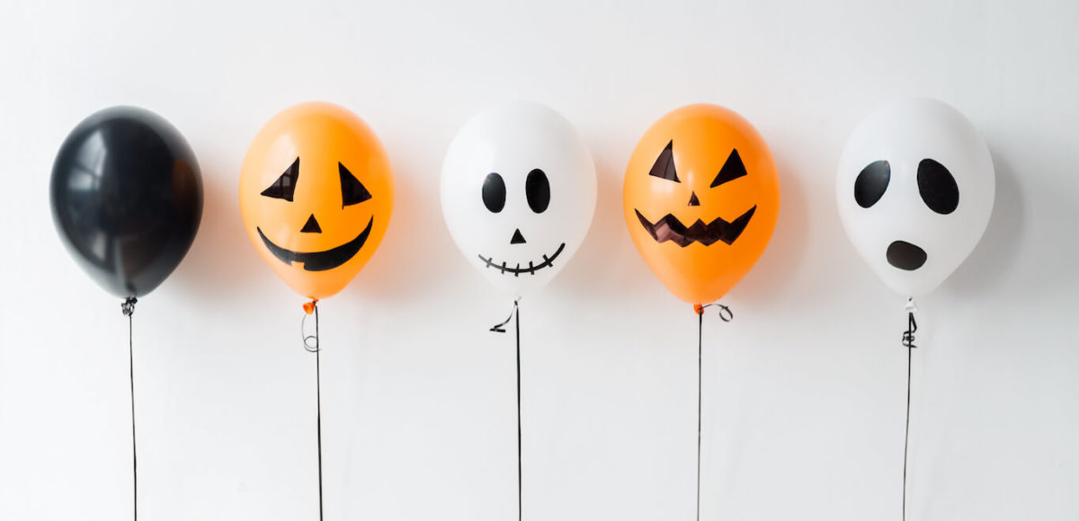 A row of black, orange, and white Halloween themed balloons on a white backdrop.