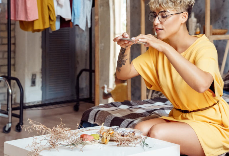Young woman in bedroom takes a photo of carefully arranged food to post on social media.