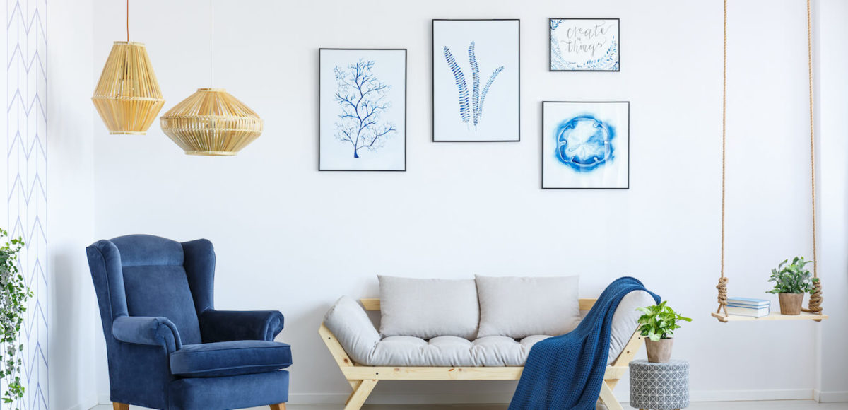 A modern living room with a neutral futon, blue armchair, and blue accents.