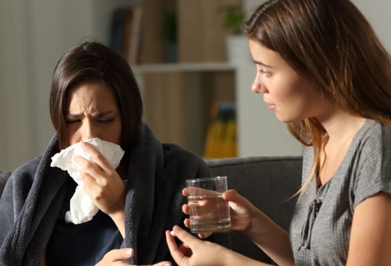 Woman giving sick and sniffly roommate medicine.