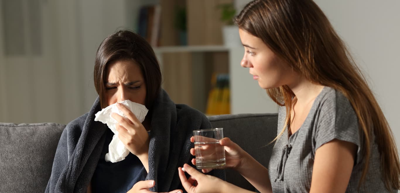 Woman giving sick and sniffly roommate medicine.