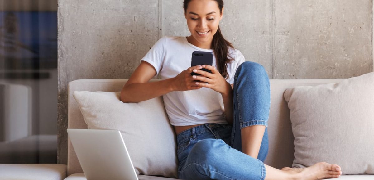 Woman sitting with phone and laptop.