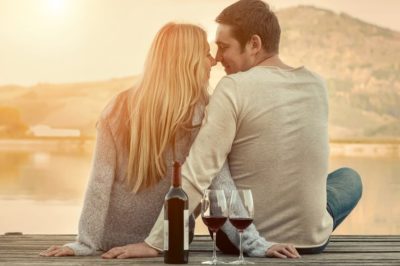 Romantic couple sitting on pier with red wine.