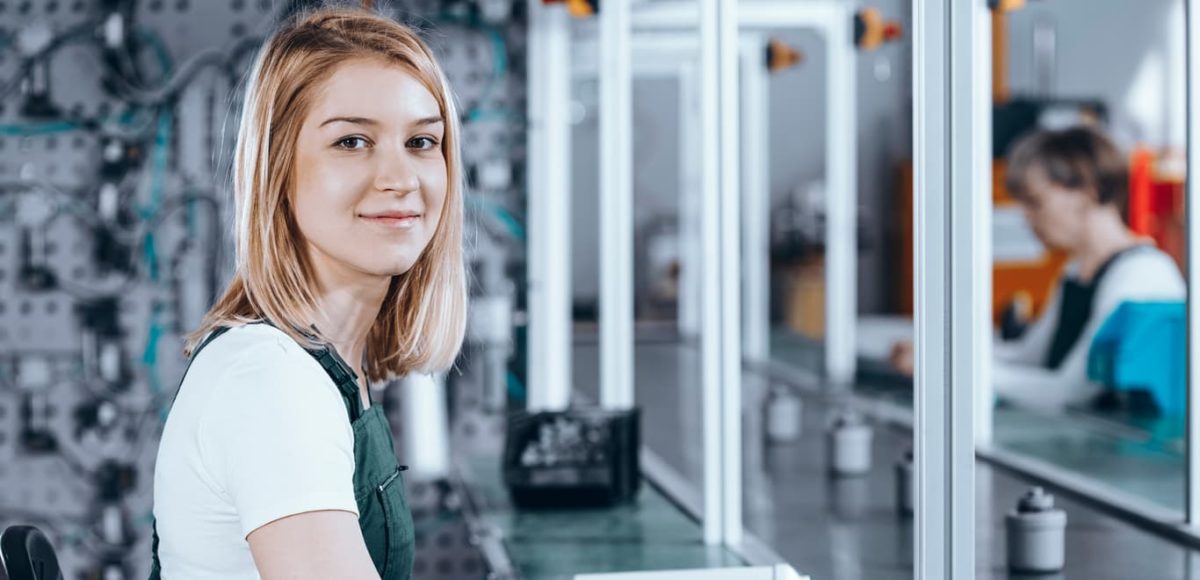 Young smiling woman in green overalls in a factory.