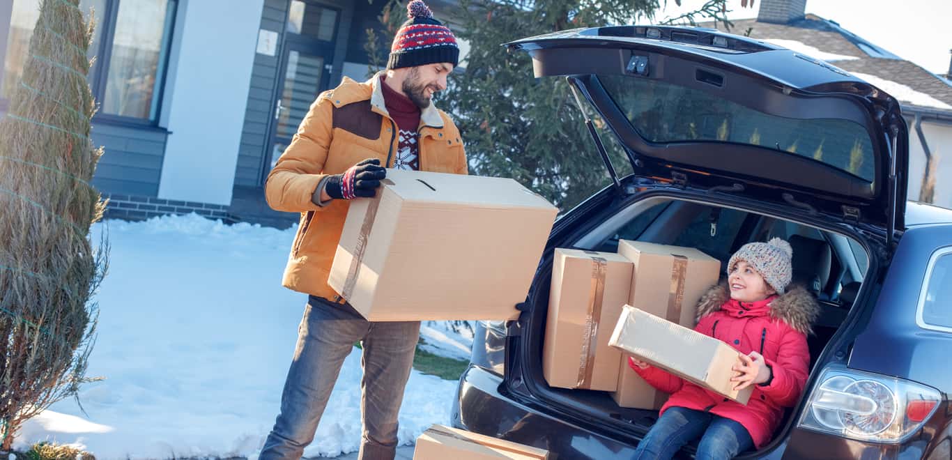 Father and daughter moving to new apartment together during winter. Holding boxes near sedan.