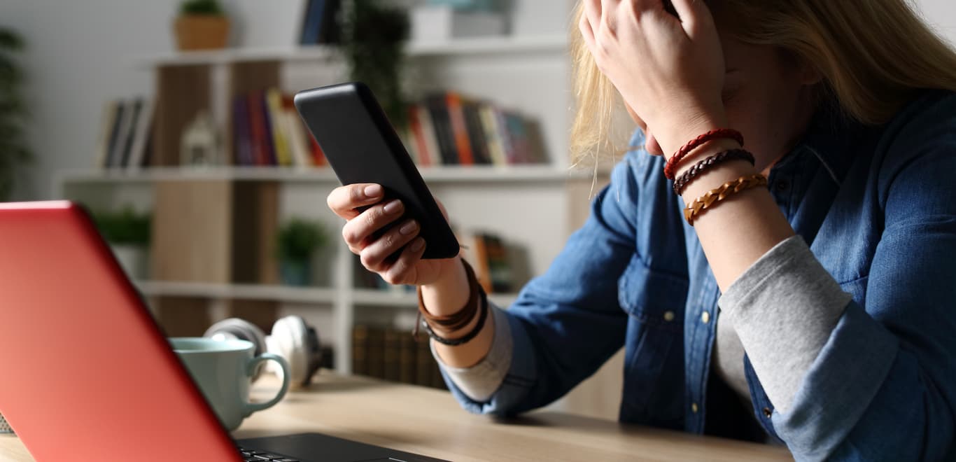 Stressed girl at desk with head in hand.