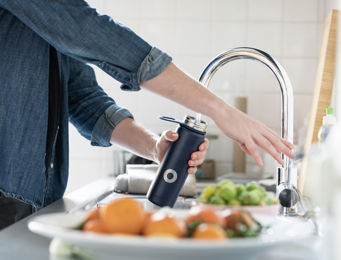 Person filling up a water bottle with kitchen faucet