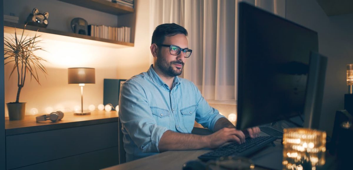 Man in blue shirt sitting in front of computer in his home office.
