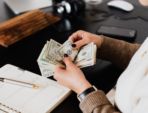 Woman counting cash with a planner on her desk