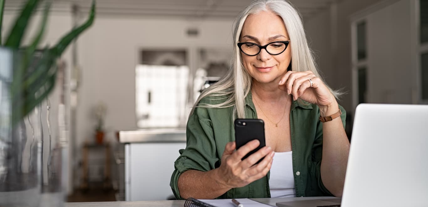 Older woman in green shirt smiling softly while looking at phone screen.