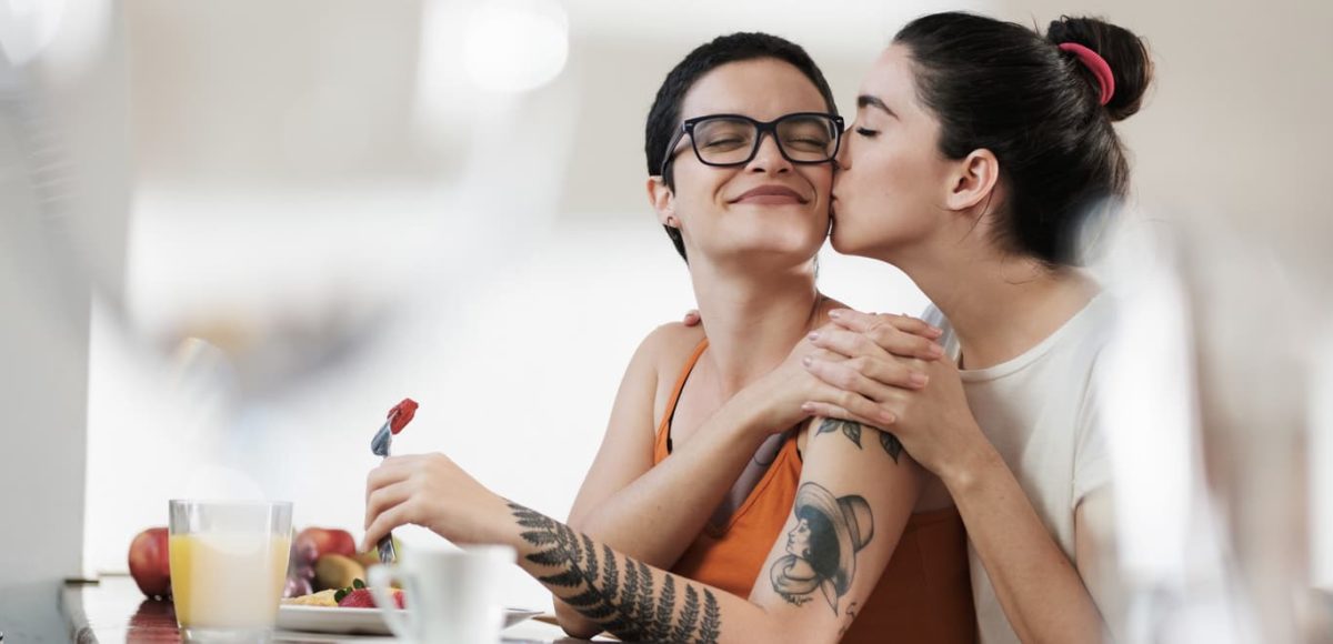 Two women embracing while one eats a fruit-based breakfast.