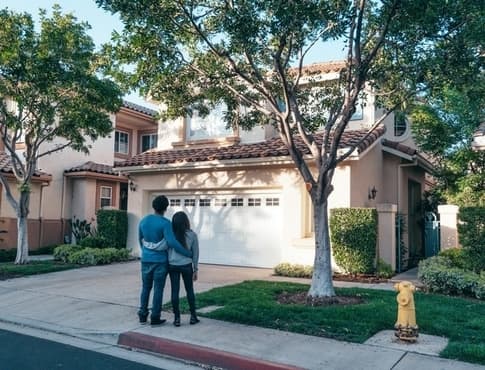 Embracing couple looking up at a two-story home.