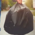 Man carrying black trash bag down suburban street.
