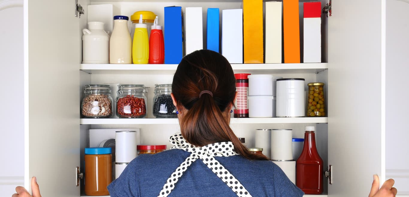 Woman in black and white polka-dot apron staring into kitchen pantry.