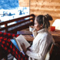 Woman on balcony in winter enjoying a book and cup of coffee.