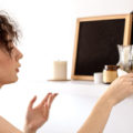Young woman dusts a well decorated shelf in her apartment to get rid of dust.