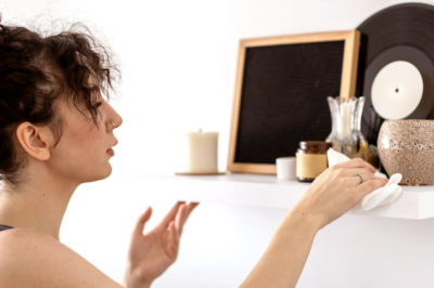 Young woman dusts a well decorated shelf in her apartment to get rid of dust.