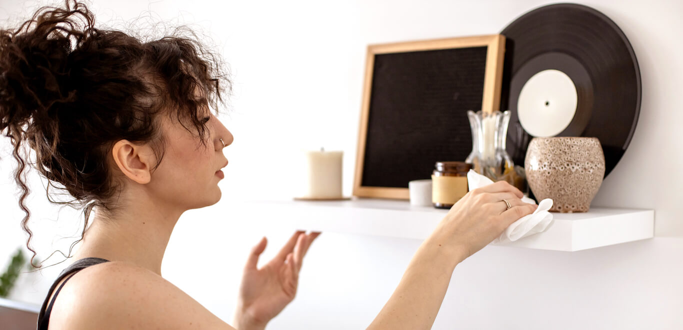 Young woman dusts a well decorated shelf in her apartment to get rid of dust.