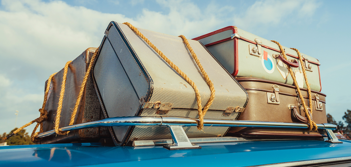 Pile of vintage bags on roof of the travel car fastened with rope moving to a new city.