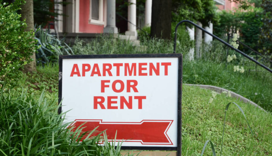 Sign outside of walk up brick apartment that says Apartment For Rent in a lush green lawn.