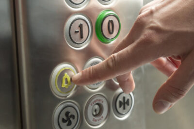 A hand reaching out to press the emergency call button on an elevator.