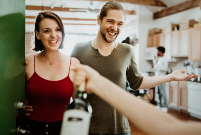 A couple hosting a housewarming party opens their door to friends arriving.
