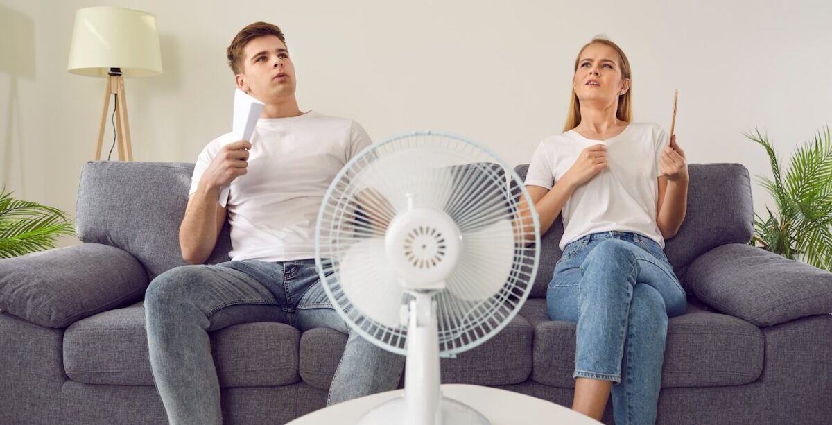A man and woman trying to cool off in front of a fan.
