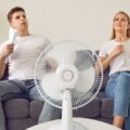 A man and woman trying to cool off in front of a fan.