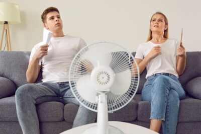 A man and woman trying to cool off in front of a fan.