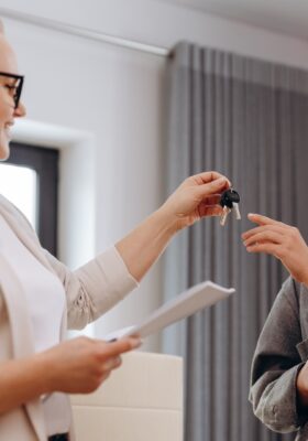 Close up young female real estate agent giving keys to happy renter, congratulating her on finding her apartment with an apartment guide